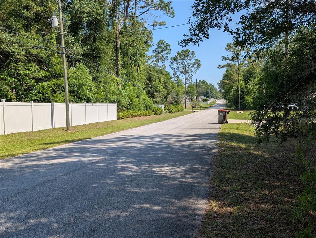 A paved residential street lined with trees, a white vinyl fence, and a trash bin — 202ND CT, DUNNELLON, FL