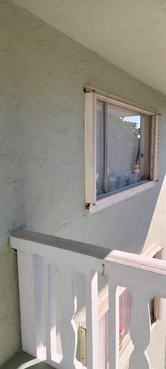 A view of a stucco exterior wall with a window and a white wooden railing — 3100 Springdale Boulevard # 317, Palm Springs FL 33461, PALM SPRINGS, FL
