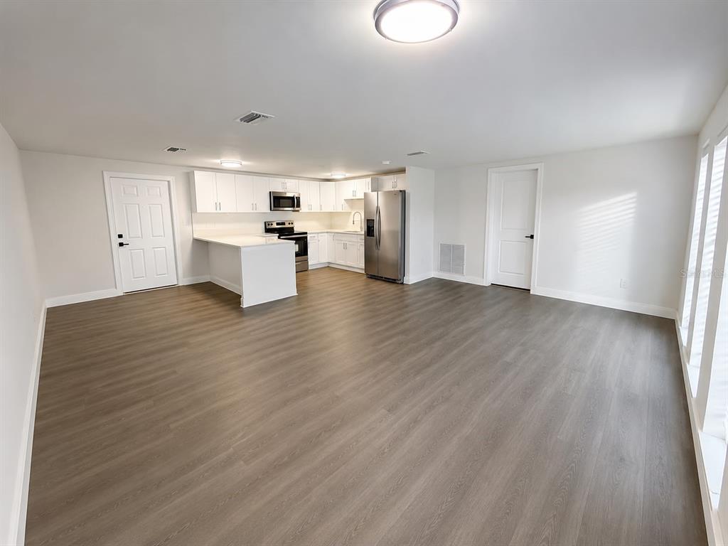 An open-concept kitchen and living area features white cabinets, stainless appliances, and wood-look flooring — 7035 PALISADE DRIVE, PORT RICHEY, FL