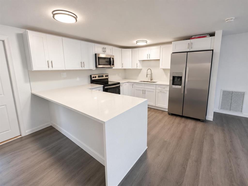 A modern kitchen features white cabinets, stainless steel appliances, and a white quartz peninsula countertop — 7035 PALISADE DRIVE, PORT RICHEY, FL