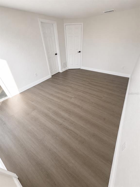 An empty room features light gray walls, dark wood-look flooring, and two white interior doors — 7035 PALISADE DRIVE, PORT RICHEY, FL