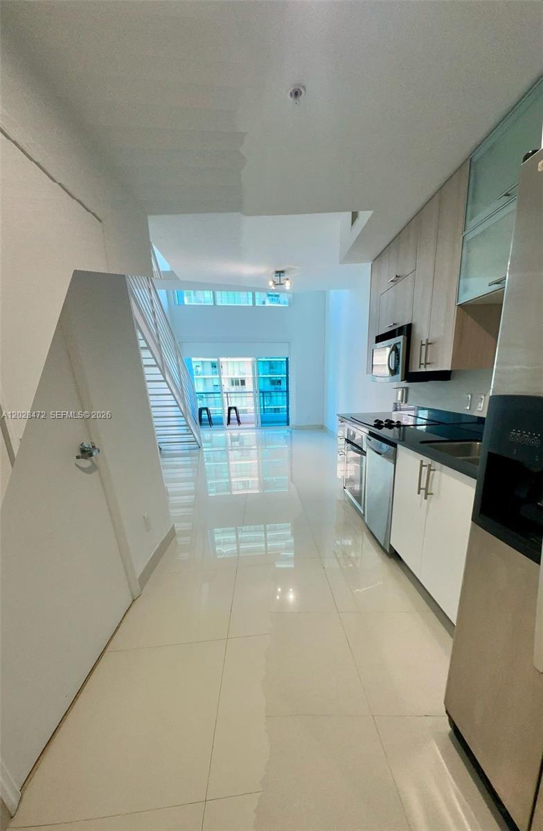 A modern kitchen with white cabinetry and tile flooring opens into a bright living area — MIAMI, FL