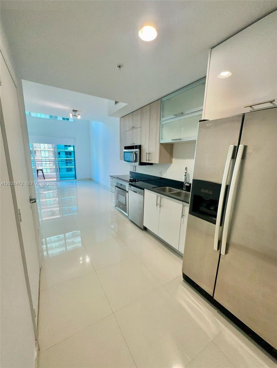 A modern kitchen features stainless steel appliances, light wood cabinetry, and white tile flooring — MIAMI, FL