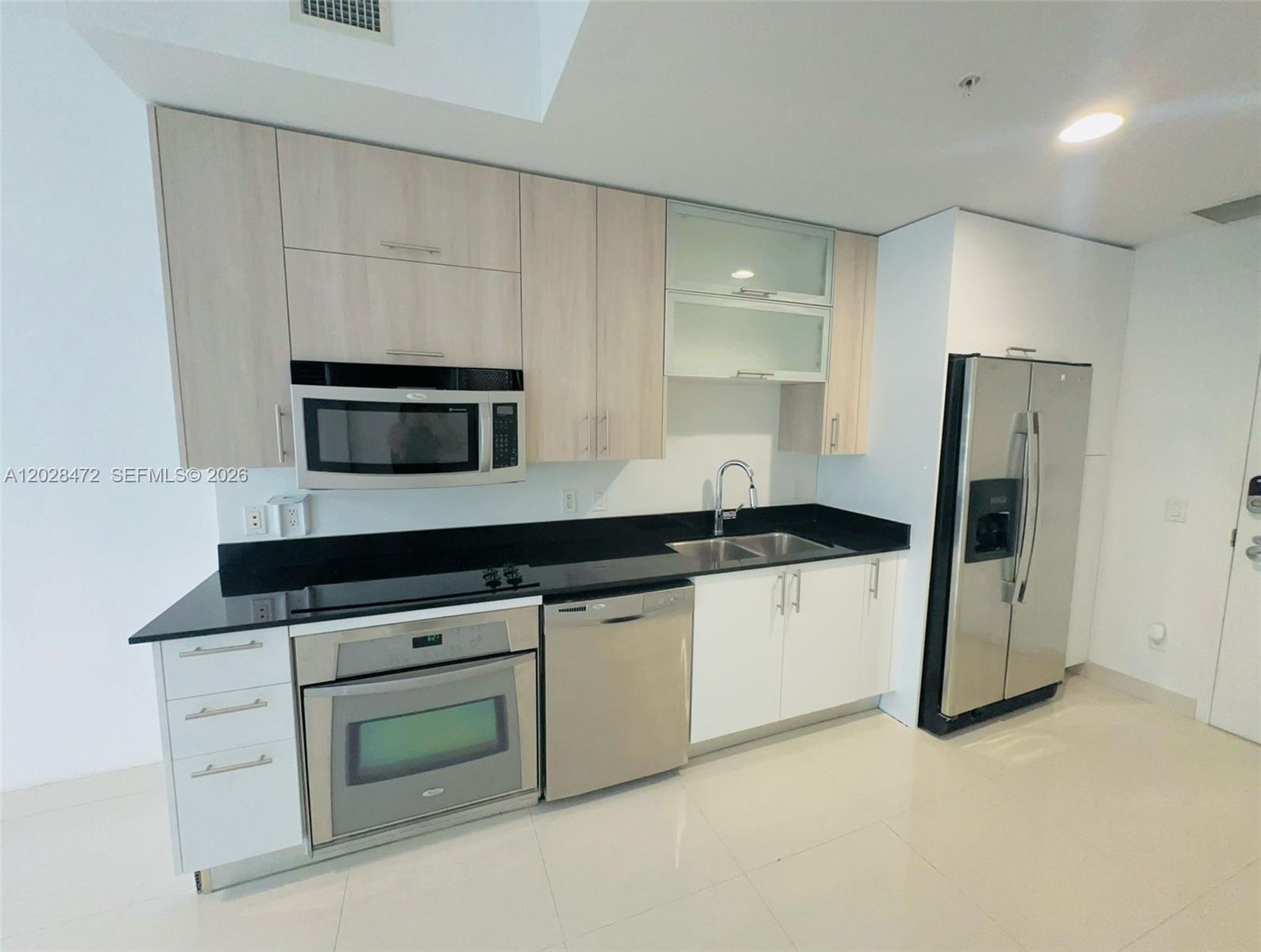 A modern kitchen features light wood cabinets, black countertops, and stainless steel appliances — MIAMI, FL