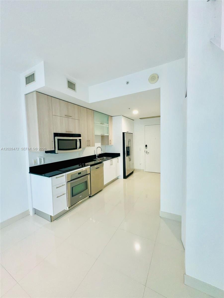 A modern kitchen features white lower cabinets, light wood upper cabinets, and black countertops — MIAMI, FL