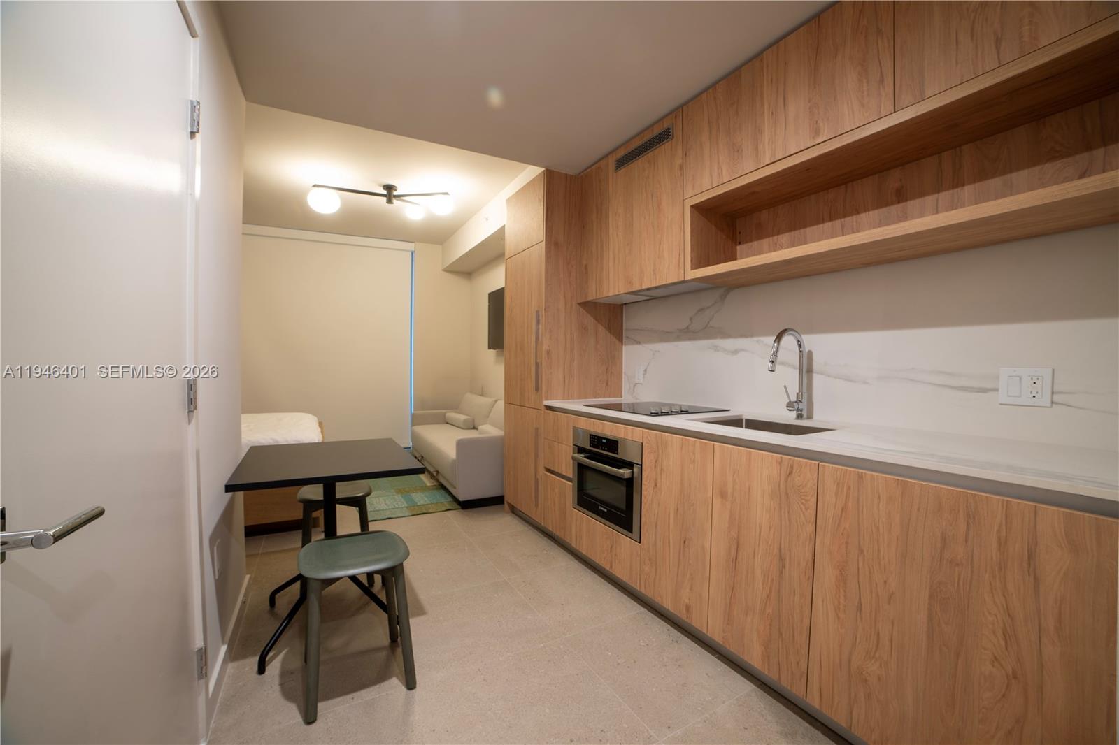 A modern studio apartment features a kitchenette with wood cabinetry and a small dining area — 11 NE 6TH # 1908, Miami FL 33132, MIAMI, FL