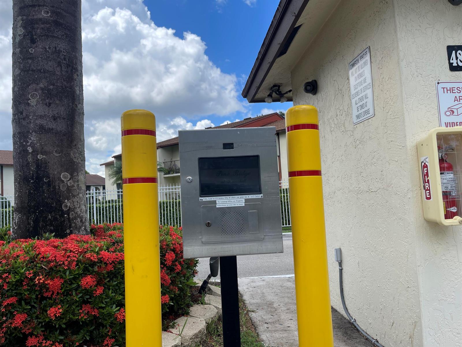 A metal gate entry keypad stands between two yellow bollards outside a building — 4857 Sable Pine Circle # B1, West Palm Beach FL 33417, WEST PALM BEACH, FL