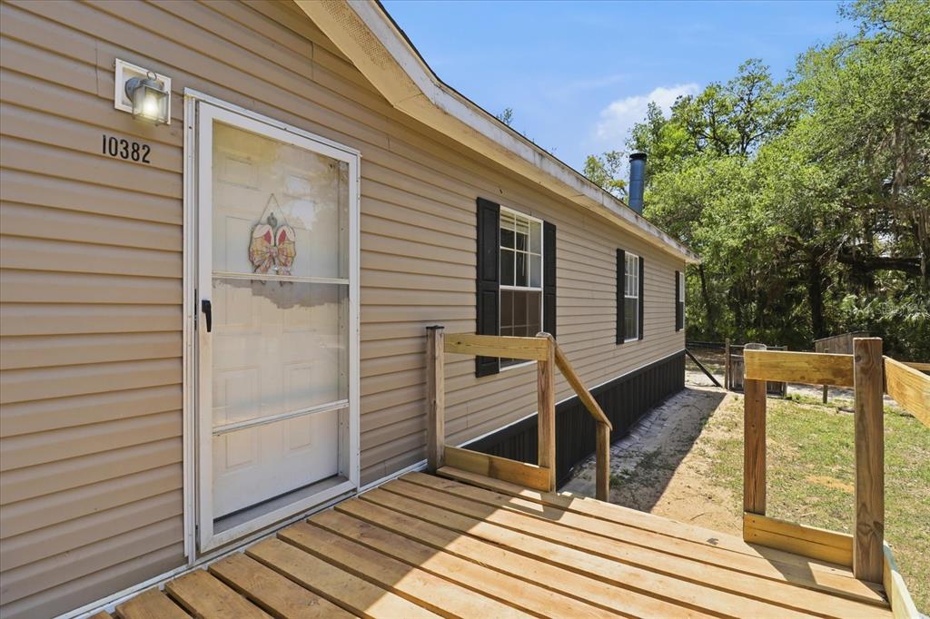 A wooden deck leads to the front door of a tan mobile home with shutters — 10382 W KILLARNEY STREET, CRYSTAL RIVER, FL