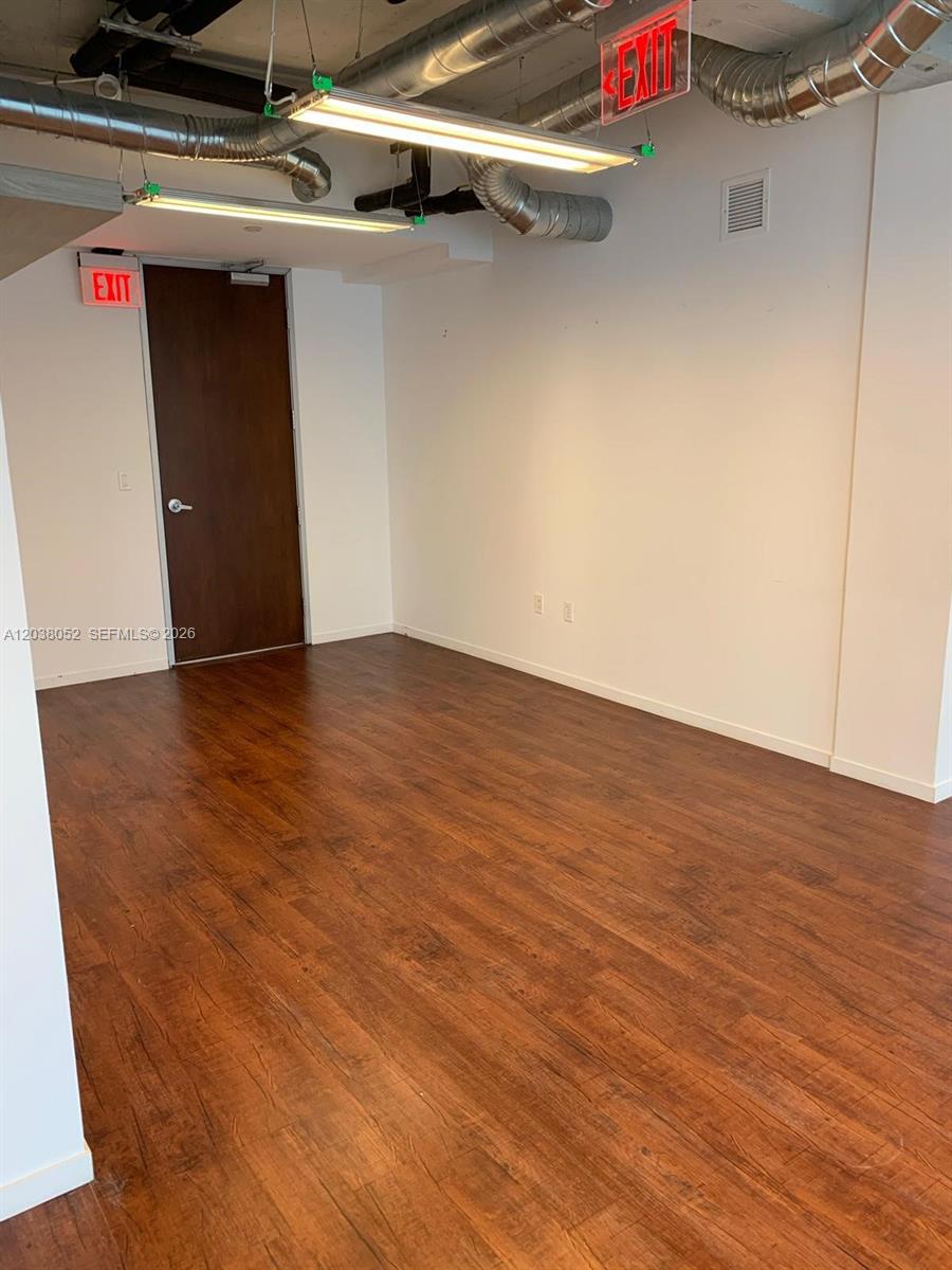 An empty office space features dark wood-look flooring, white walls, and exposed industrial ceiling ducts — 14 NE 1st Ave # Q, Miami FL 33132, MIAMI, FL