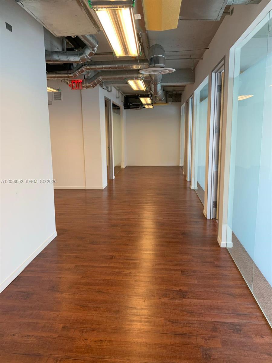 A hallway with wood-look flooring leads to an office space with exposed ceiling ductwork — 14 NE 1st Ave # Q, Miami FL 33132, MIAMI, FL