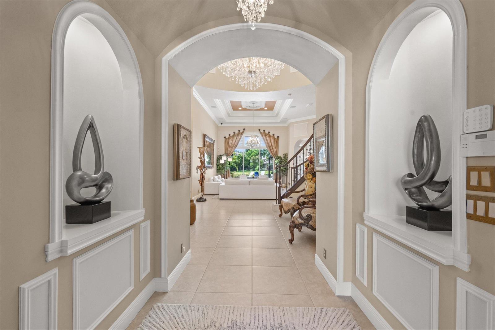 A grand foyer features arched niches with sculptures, tile flooring, and a view into the living room — 10771 Versailles Boulevard, Wellington FL 33449, WELLINGTON, FL