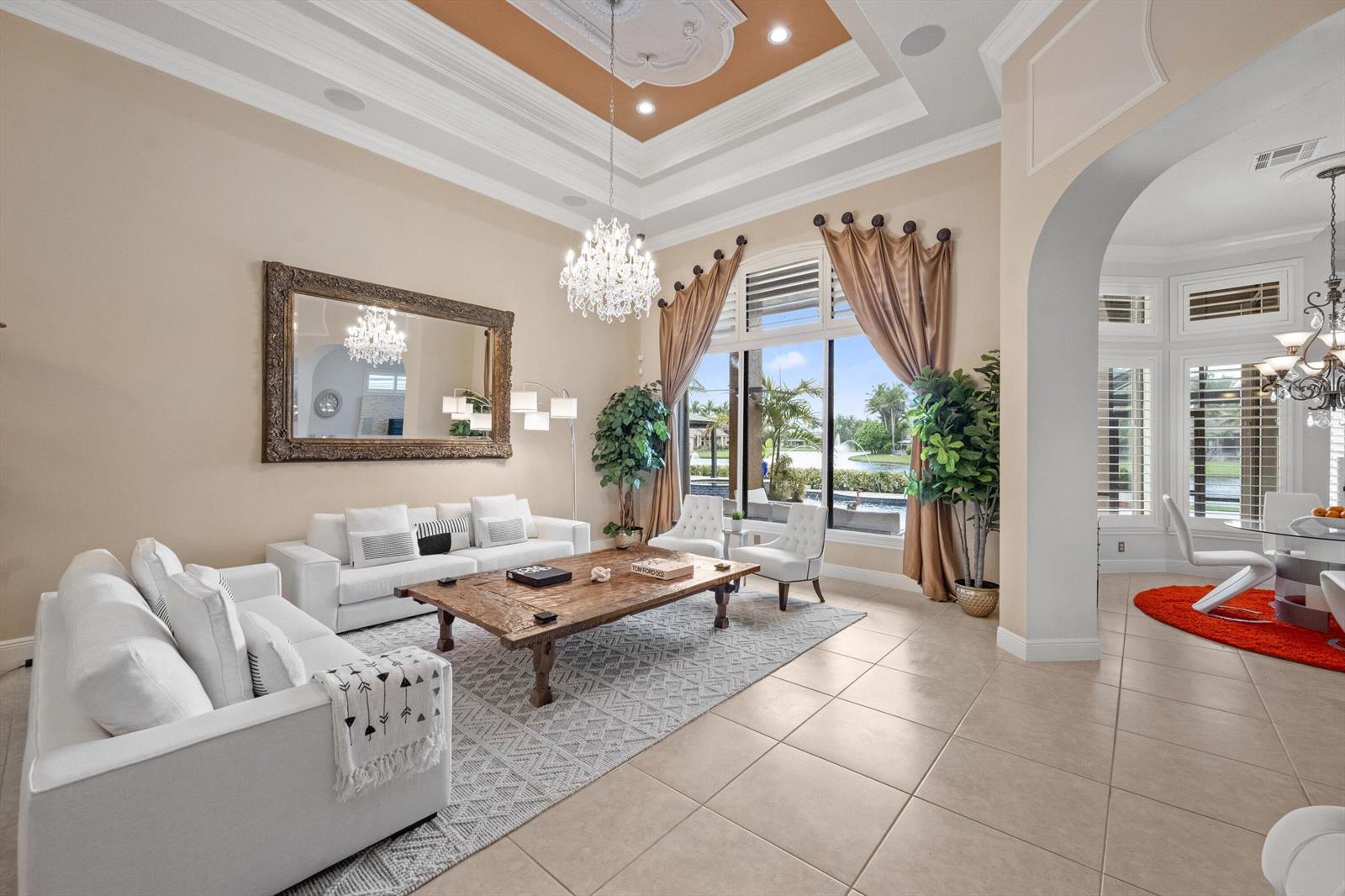 A spacious living room features white sofas, a wooden coffee table, and a large mirror — 10771 Versailles Boulevard, Wellington FL 33449, WELLINGTON, FL