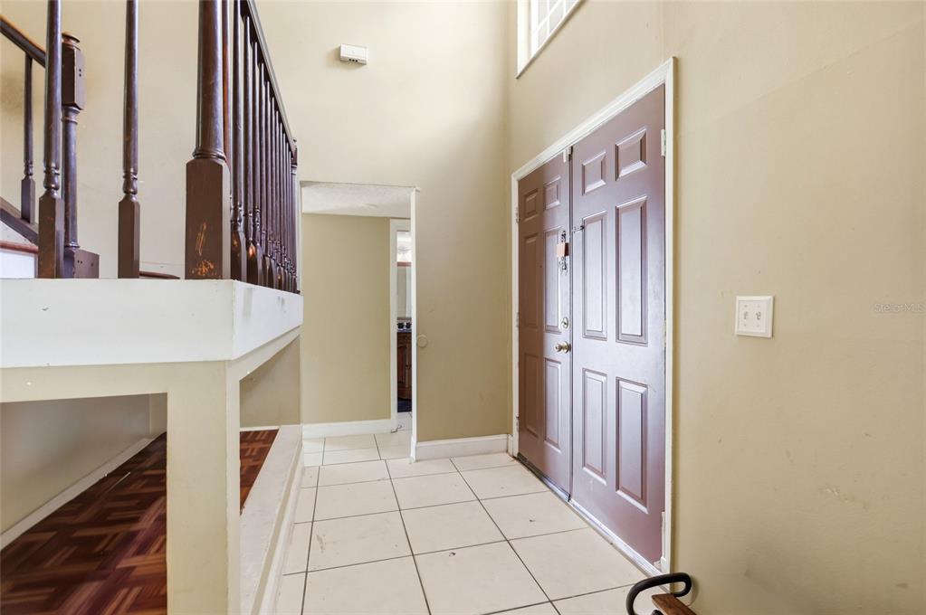 An entryway features a tiled floor, a brown double door, and a wooden staircase railing — 1071 SUMMER LAKES DRIVE, ORLANDO, FL