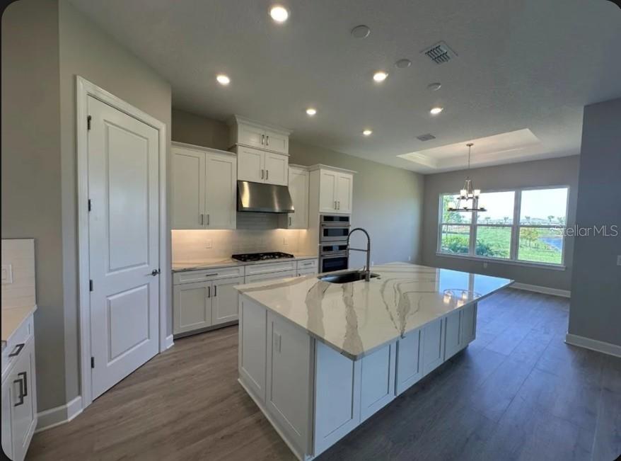 A modern kitchen features white cabinetry, a large marble-topped island, and stainless steel appliances — 998 TASSLEFLOWER TRAIL, ST CLOUD, FL