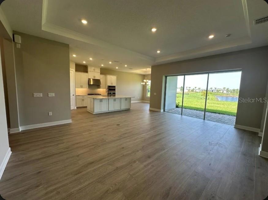 An open-concept kitchen and living area with wood-look flooring and sliding glass doors to outdoors — 998 TASSLEFLOWER TRAIL, ST CLOUD, FL