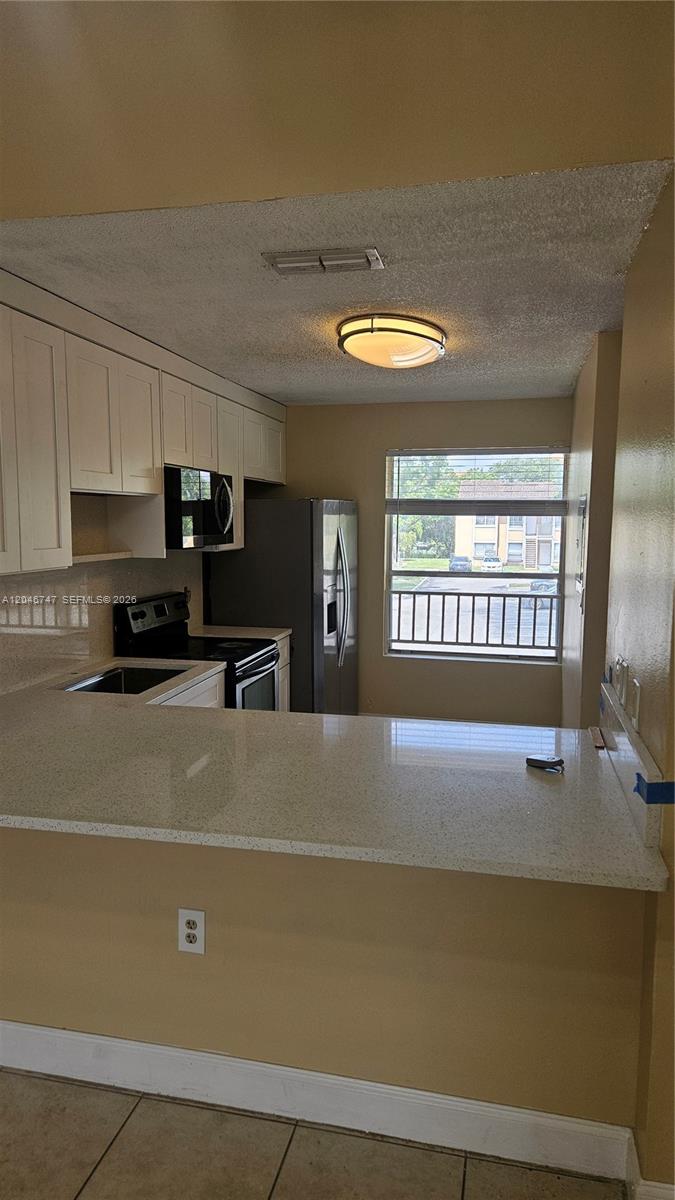 A kitchen features white cabinets, stainless steel appliances, and a light-colored countertop breakfast bar — 8039 SW 21st Ct # 8039, Miramar FL 33025, MIRAMAR, FL