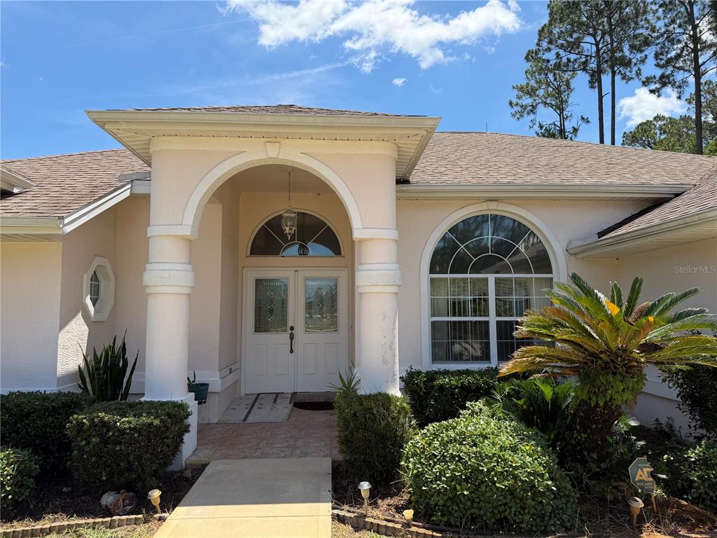 The exterior of a beige house features a covered entryway with columns and arched windows — 78 BARRINGTON DRIVE, PALM COAST, FL