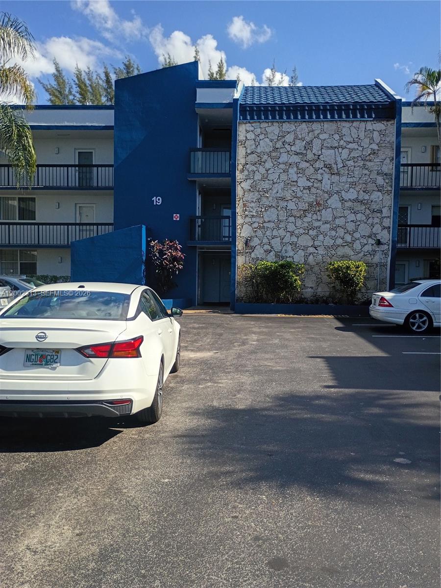 A three-story apartment building exterior features blue walls, a stone facade, and a parking lot — 3040 Holiday Springs Blvd # 110, Margate FL 33063, MARGATE, FL