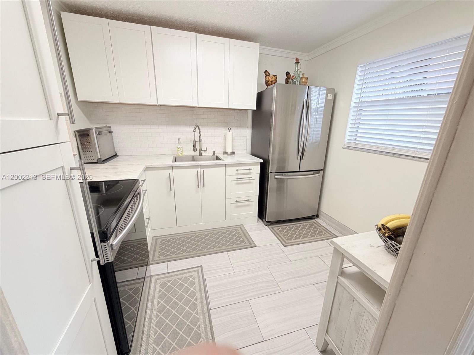 A kitchen features white cabinets, stainless steel appliances, a subway tile backsplash, and light flooring — 3040 Holiday Springs Blvd # 110, Margate FL 33063, MARGATE, FL