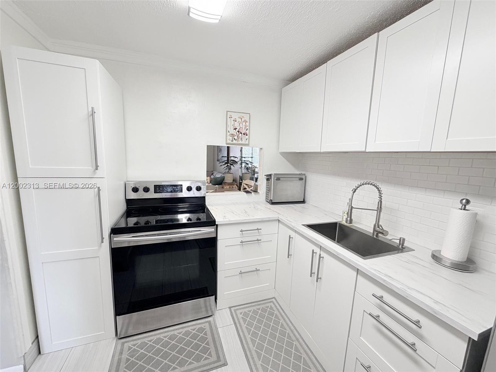 A modern kitchen features white cabinets, marble-look countertops, a stainless steel stove, and subway tile — 3040 Holiday Springs Blvd # 110, Margate FL 33063, MARGATE, FL