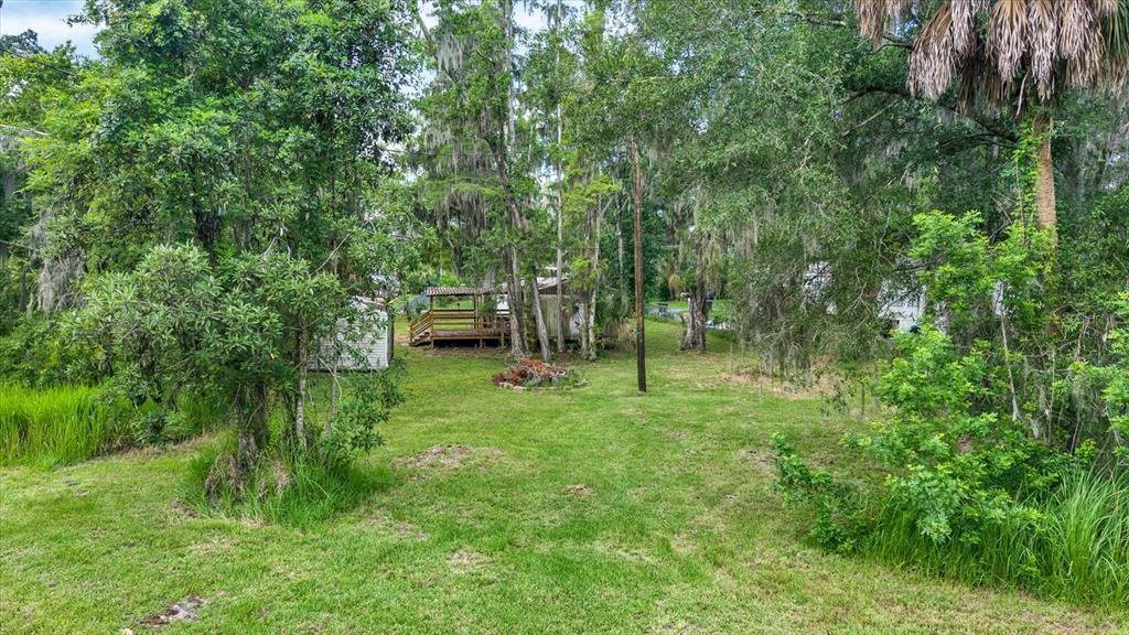 A grassy backyard features a small shed, a wooden deck, and mature trees — 3913 ALAFIA BOULEVARD, BRANDON, FL