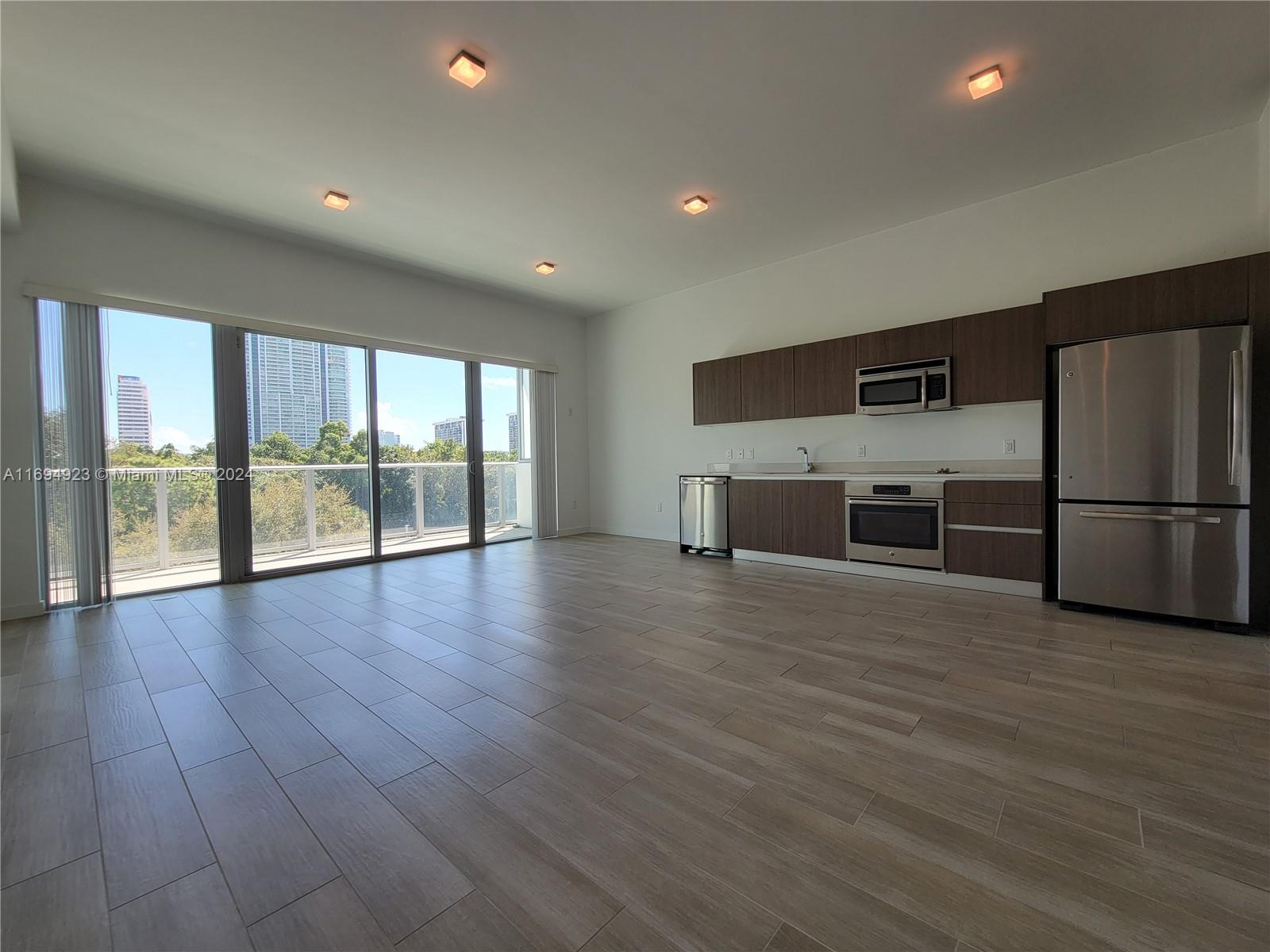 An open-concept kitchen and living area features wood-look tile floors and a balcony view — 1600 SW 1 Ave # 411, Miami FL 33129, MIAMI, FL