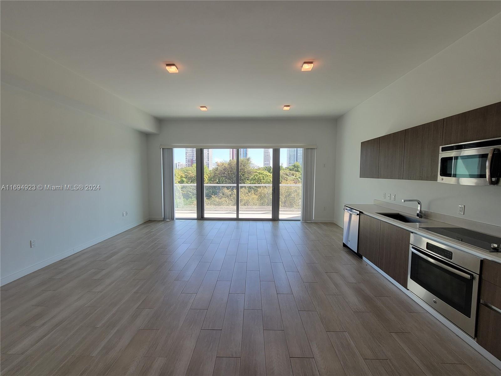 An open-concept living area features light wood-look flooring, a modern kitchen, and a balcony view — 1600 SW 1 Ave # 411, Miami FL 33129, MIAMI, FL