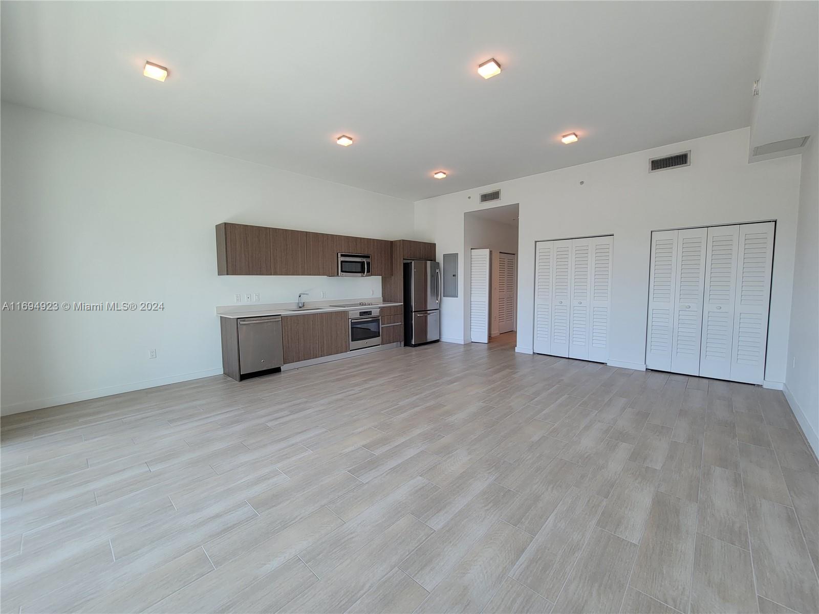 An open-concept kitchen features wood-tone cabinetry, stainless steel appliances, and light-colored tile flooring — 1600 SW 1 Ave # 411, Miami FL 33129, MIAMI, FL