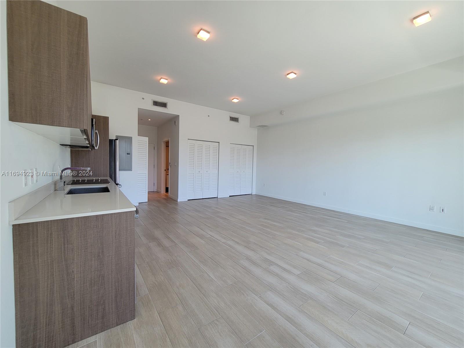 An open-concept kitchen and living area features wood-tone cabinetry, light tile flooring, and white walls — 1600 SW 1 Ave # 411, Miami FL 33129, MIAMI, FL