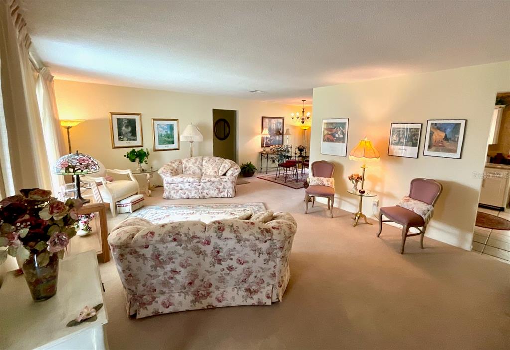 A living room with floral sofas, beige carpeting, and several framed pictures on the walls — 3807 99TH TERRACE N, PINELLAS PARK, FL