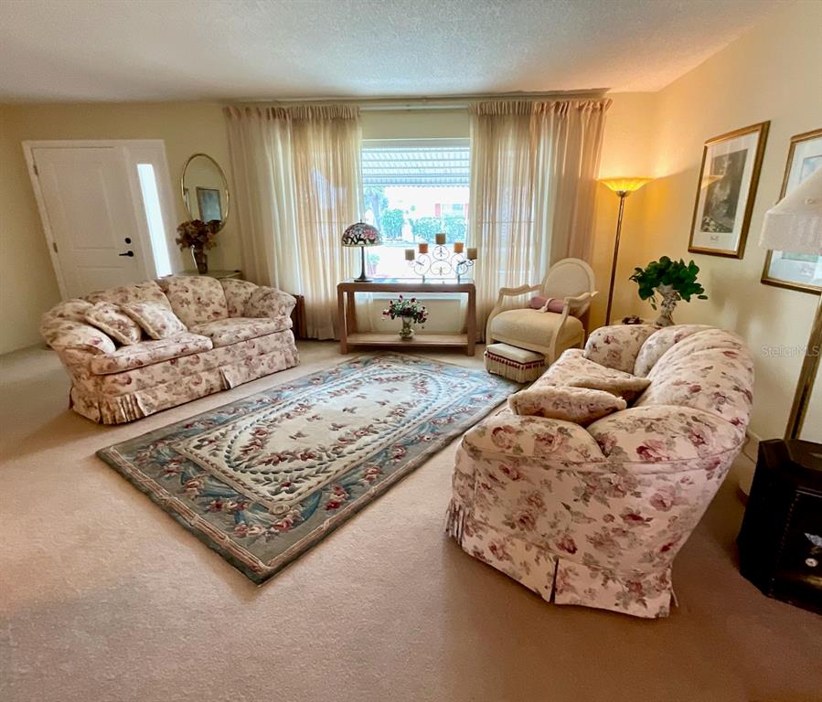A living room features two floral sofas, a patterned area rug, and a window with curtains — 3807 99TH TERRACE N, PINELLAS PARK, FL