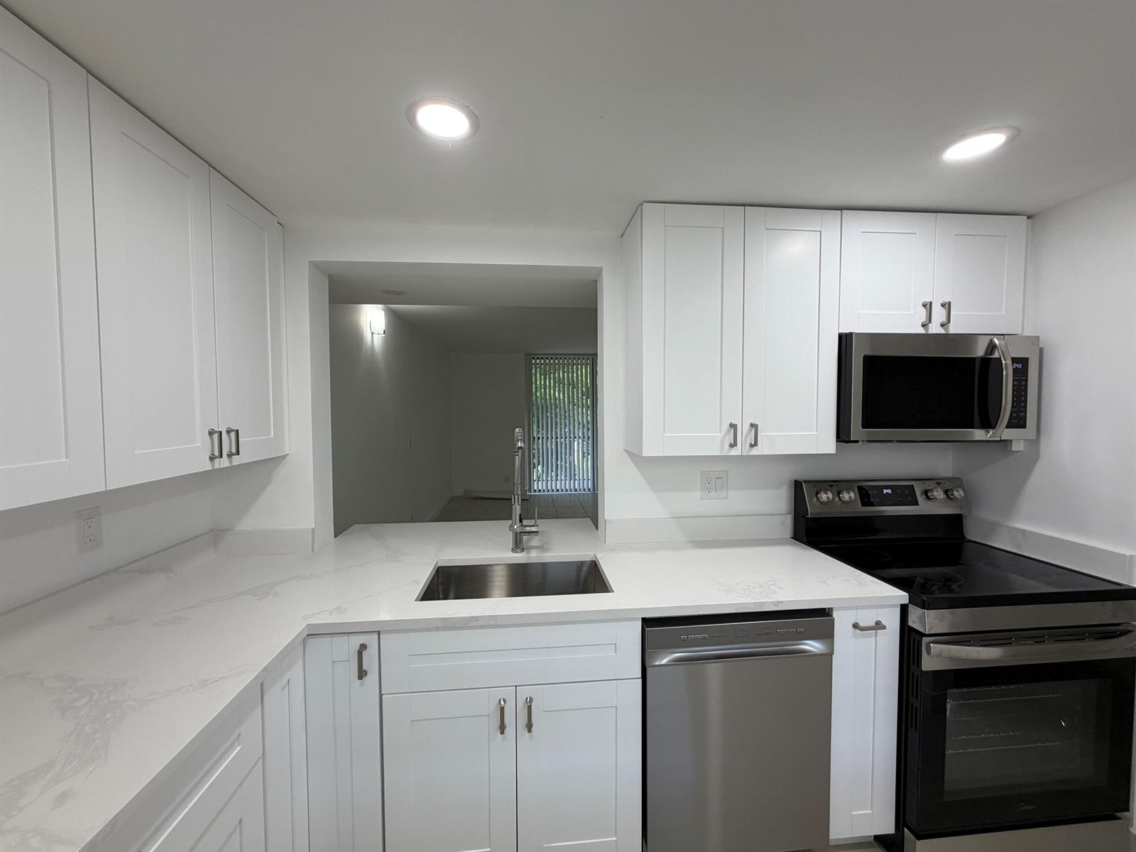 A modern kitchen features white shaker cabinets, white marble-look countertops, and a stainless steel sink — 5220 Las Verdes Circle # 317, Delray Beach FL 33484, DELRAY BEACH, FL