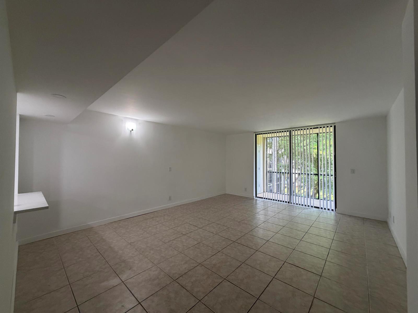 An empty living room with light tile flooring, white walls, and a large sliding glass door — 5220 Las Verdes Circle # 317, Delray Beach FL 33484, DELRAY BEACH, FL