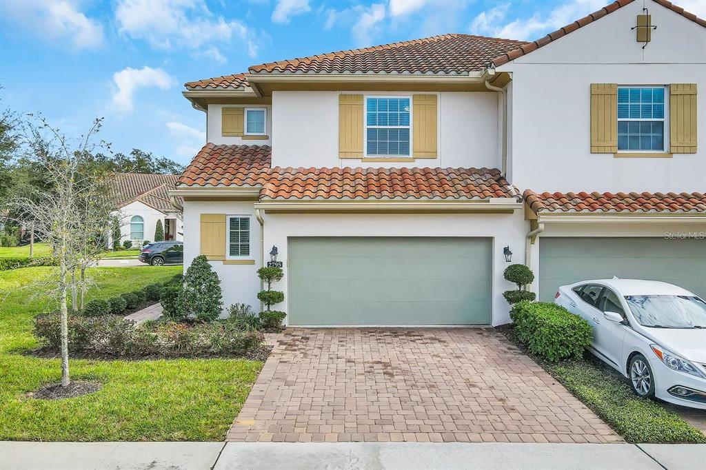 A two-story townhouse exterior features a paved driveway, a green garage door, and tiled roofing — 2795 BOLZANO DRIVE, APOPKA, FL