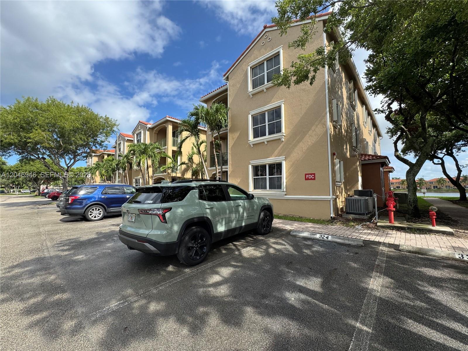 A light green SUV is parked in front of a three-story tan apartment building — 6360 NW 114th Ave # 224, Doral FL 33178, DORAL, FL