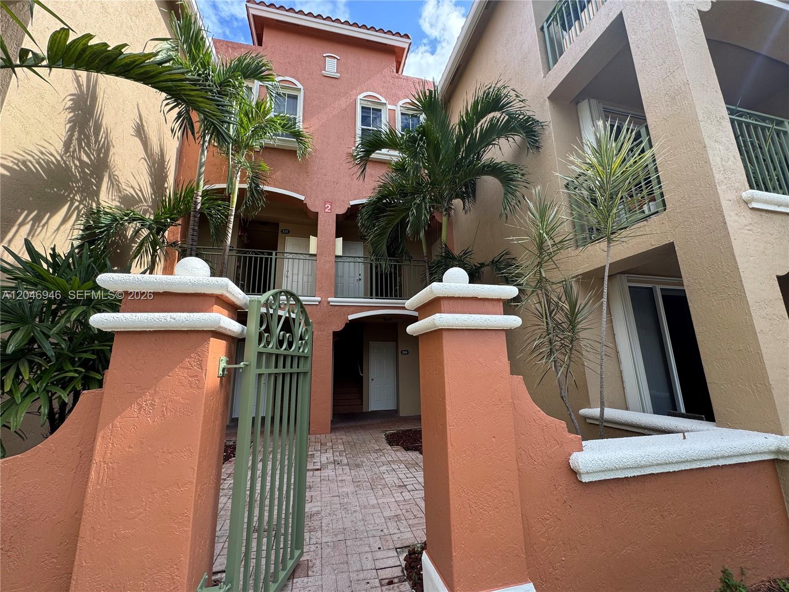A paved walkway leads through a gate toward the entrance of a multi-story stucco building — 6360 NW 114th Ave # 224, Doral FL 33178, DORAL, FL