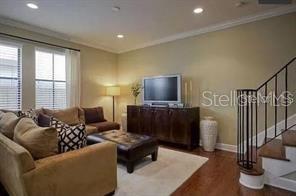 A living room features a tan sofa, a television on a dark cabinet, and stairs — 107 S PACKWOOD AVENUE UNIT D, TAMPA, FL