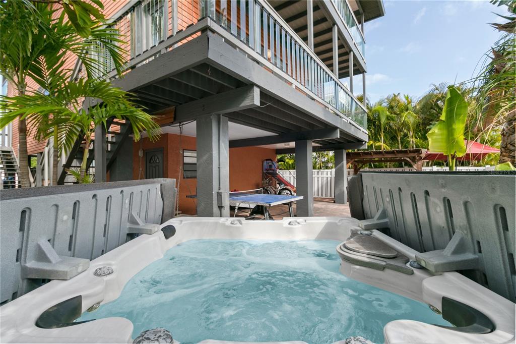 A hot tub sits on a patio beneath a raised deck with a ping pong table — 2511 AVENUE C UNIT West, BRADENTON BEACH, FL