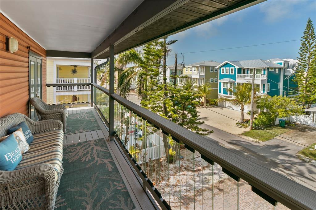 A covered balcony features wicker furniture and a view of neighboring houses and palm trees — 2511 AVENUE C UNIT West, BRADENTON BEACH, FL