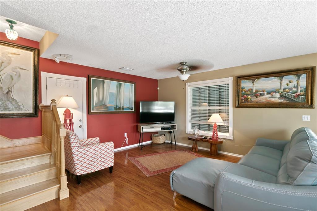 A living room features red and tan walls, wood flooring, a television, and a blue sofa — 2511 AVENUE C UNIT West, BRADENTON BEACH, FL