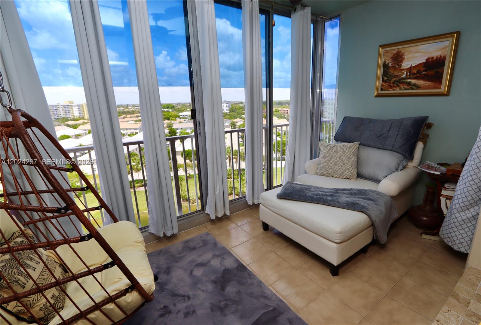 A sunroom features a hanging chair, a chaise lounge, and floor-to-ceiling windows overlooking a neighborhood — 3850 Washington St # 1010, Hollywood FL 33021, HOLLYWOOD, FL