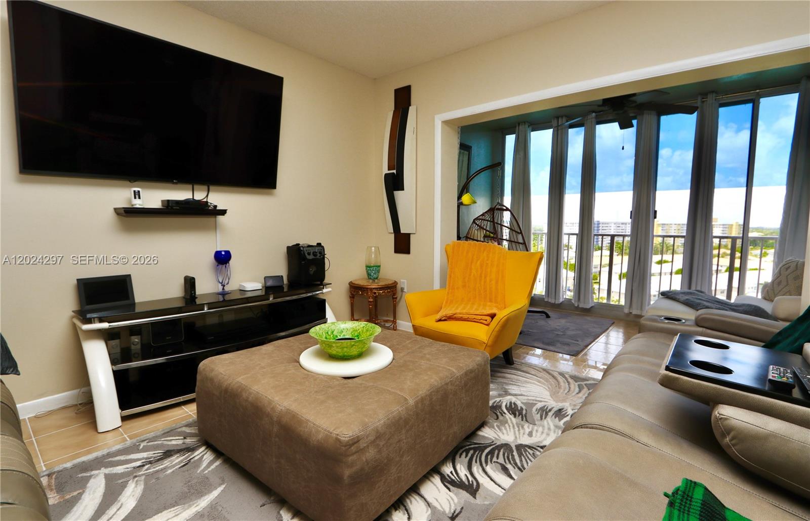 A living room features a large television, a yellow armchair, and a balcony view — 3850 Washington St # 1010, Hollywood FL 33021, HOLLYWOOD, FL