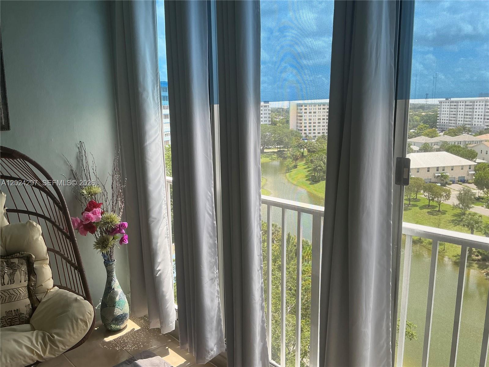 A room with a hanging chair, a floral vase, and sliding doors overlooking a lake — 3850 Washington St # 1010, Hollywood FL 33021, HOLLYWOOD, FL