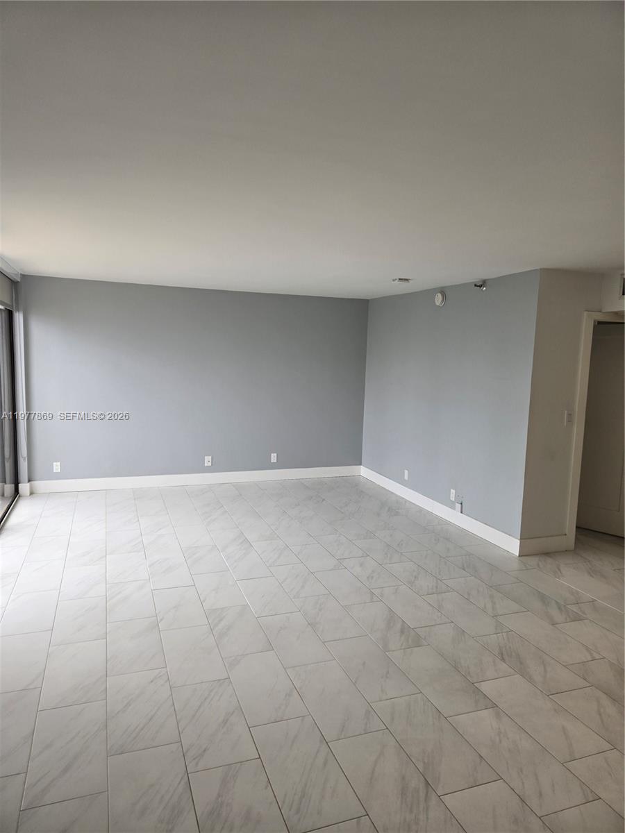 An empty room features light gray walls, white baseboards, and white marble-look tile flooring — SUNNY ISLES BEACH, FL