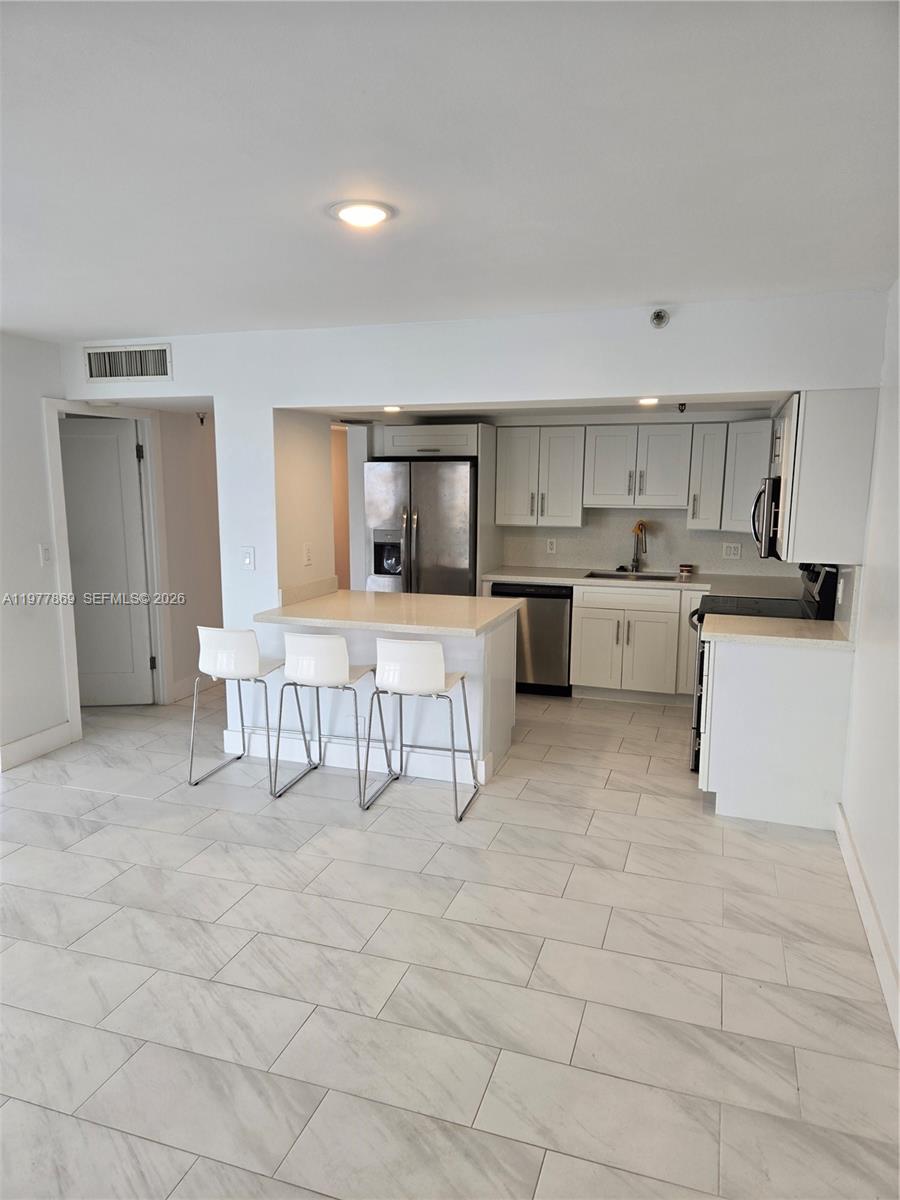 A kitchen features white cabinets, stainless steel appliances, a breakfast bar, and marble-look tile flooring — SUNNY ISLES BEACH, FL