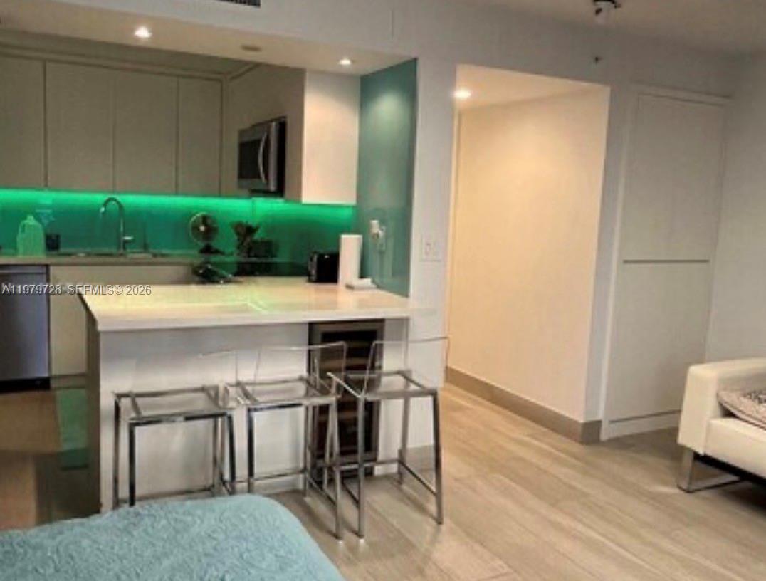 A kitchen features white cabinets, a green backsplash, and a breakfast bar with clear stools — 2457 Collins Ave # 1605, Miami Beach FL 33140, MIAMI BEACH, FL