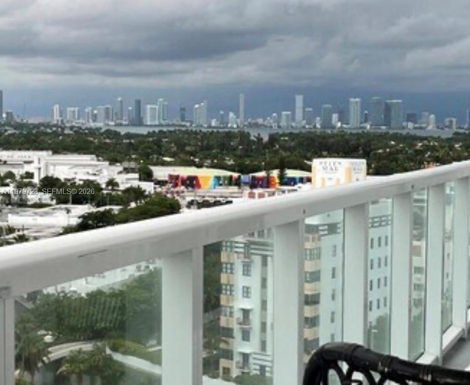 A balcony view overlooking a suburban area with a distant city skyline under cloudy skies — 2457 Collins Ave # 1605, Miami Beach FL 33140, MIAMI BEACH, FL