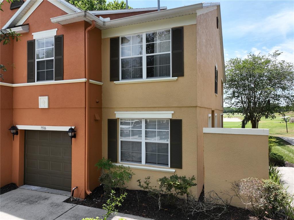 An exterior view of a two-story townhouse with a balcony, patio, and landscaped yard — 7586 ASSEMBLY LANE, REUNION, FL