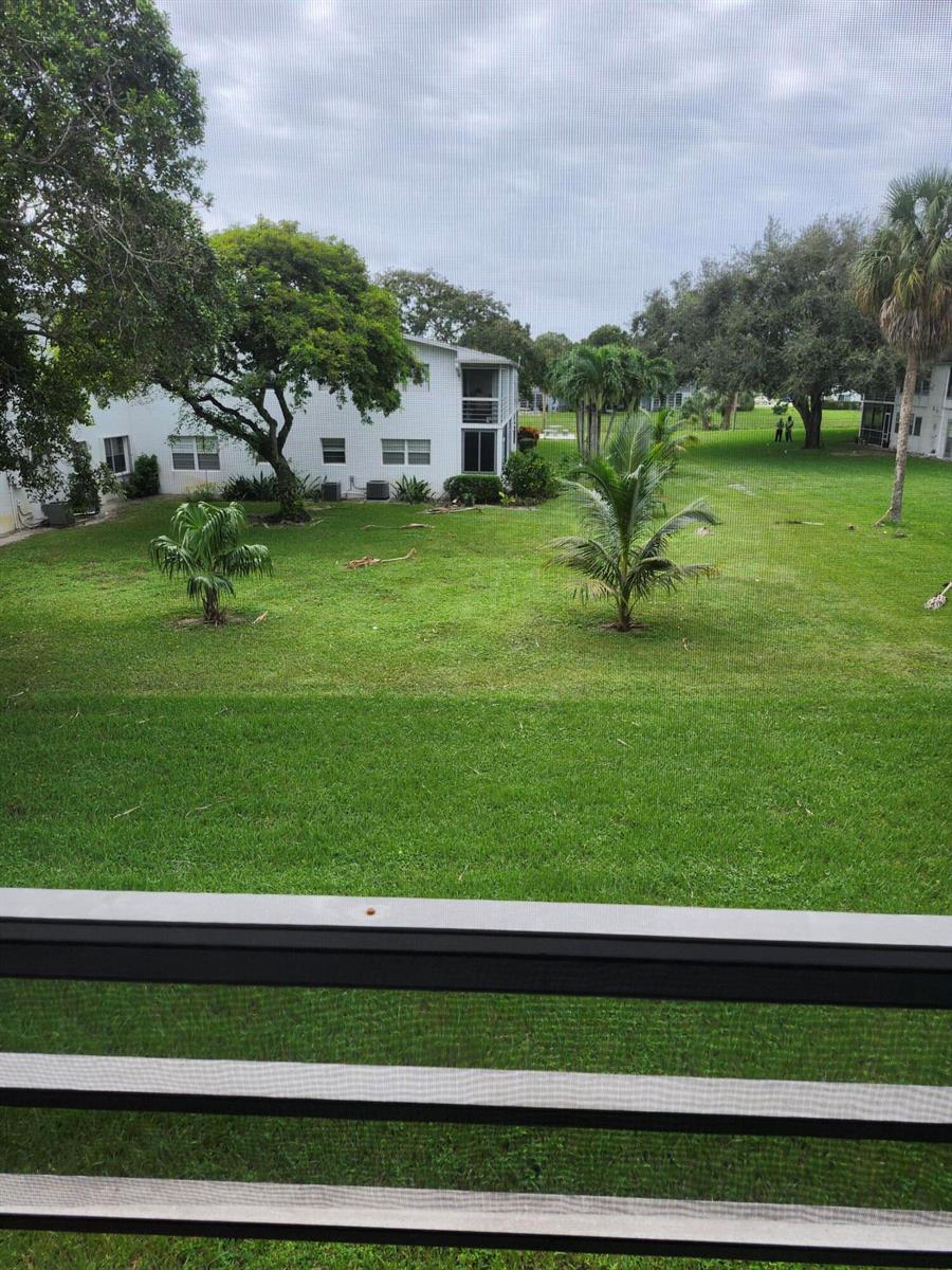 A view from a screened balcony overlooking a grassy courtyard with trees and apartment buildings — 272 Tilford M, Deerfield Beach FL 33442, DEERFIELD BEACH, FL