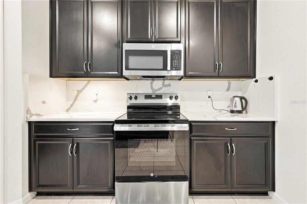 A kitchen features dark wood cabinets, stainless steel appliances, and white marble-patterned countertops — 1045 DUDLEY DRIVE, KISSIMMEE, FL
